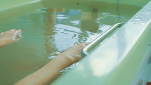 Feliz joven mujer relajarse en aguas termales y el uso de la mano para rescatar el agua, la mujer está acostada en el baño — Vídeo de stock