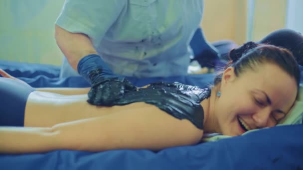 Ontspannen jonge vrouw liggend op kuuroord voor lichaamsmassage met modder en kruiden door massagetherapeut in een luxe kuuroord. — Stockvideo