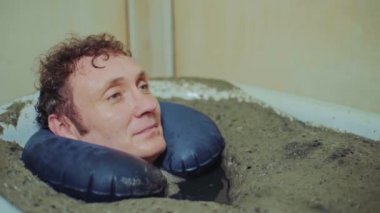 Adam terapi amaçlı çamur banyosunda uzanıyor, rahatlıyor, giyiniyor.