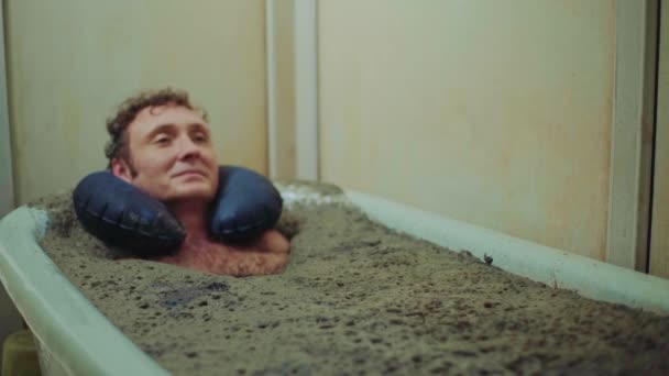 Чоловік лежить у терапевтичній грязьовій ванні, релаксація — стокове відео