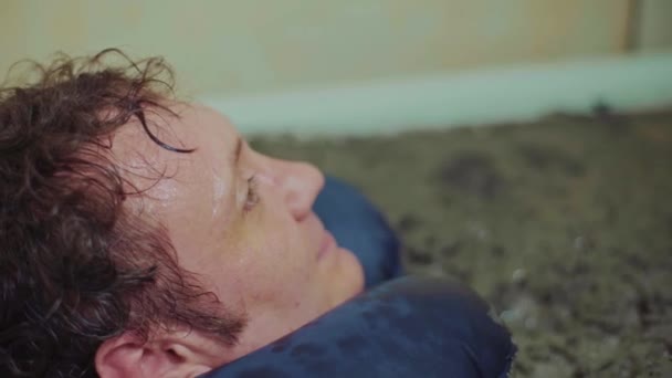 Mężczyzna leży w terapeutycznej kąpieli błotnej, relaks, clouse się — Wideo stockowe