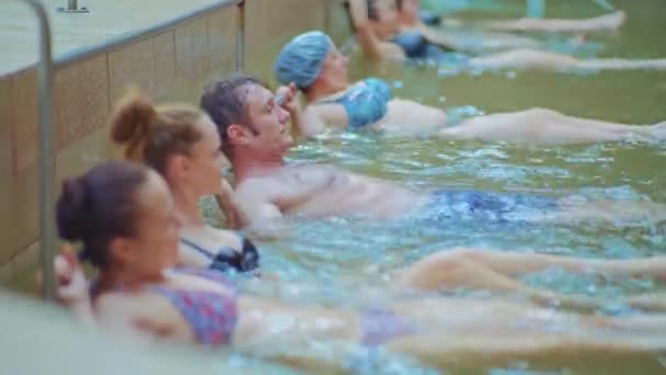 Vista lateral - personas de raza mixta se encuentran en la piscina con agua durante los ejercicios en aeróbic acuático — Vídeo de stock