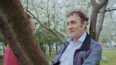 Parkta konuşan orta yaşlı bir çift, ağacın altında çiçek açan beyaz bir çift, el ele tutuştular.