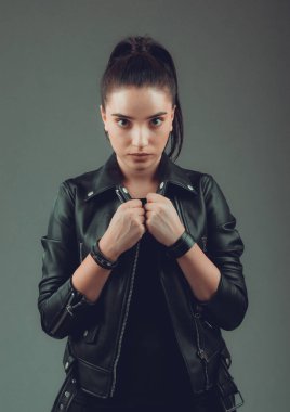 Gri arka planda siyah deri ceketli güzel bir kadının portresi.