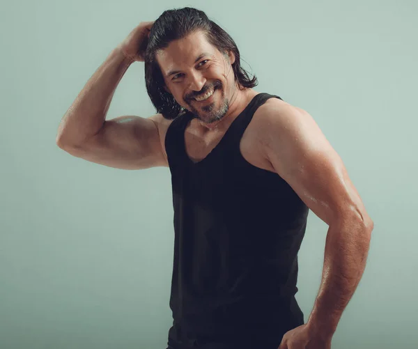 Stüdyo çekiminde yırtık kaslı gövde üzerinde koyu renk tanktop giyen erkek vücut geliştirici.