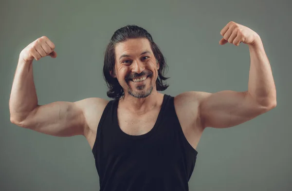 Stüdyo çekiminde yırtık kaslı gövde üzerinde koyu renk tanktop giyen erkek vücut geliştirici.