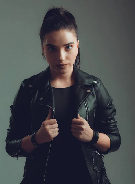 Gri arka planda siyah deri ceketli güzel bir kadının portresi.