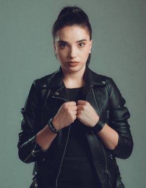 Gri arka planda siyah deri ceketli güzel bir kadının portresi.