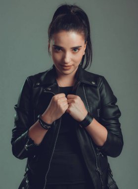 Gri arka planda siyah deri ceketli güzel bir kadının portresi.