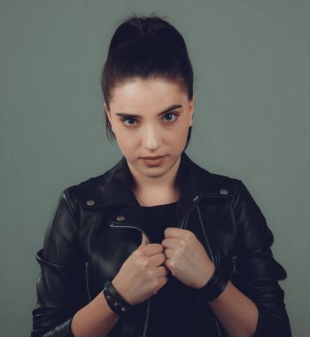 Gri arka planda siyah deri ceketli güzel bir kadının portresi.