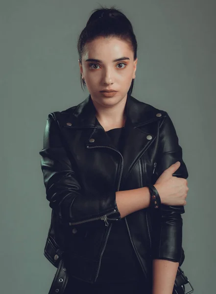 Gri arka planda siyah deri ceketli güzel bir kadının portresi.