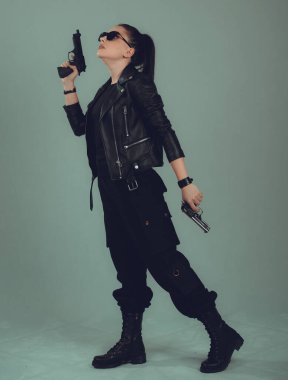 Siyah ceketli, gözlerinde siyah gözlüklerle silahlı seksi bir askeri kadının fotoğrafı.,