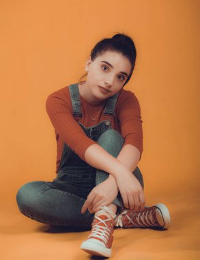 Kırmızı kazaklı, mavi tulumlu, yerde oturan güzel bir manken.,