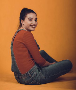 Kırmızı kazaklı, mavi tulumlu, yerde oturan güzel bir manken.,