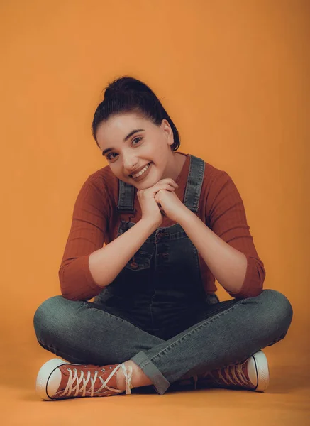 Kırmızı kazaklı, mavi tulumlu, yerde oturan güzel bir manken.,