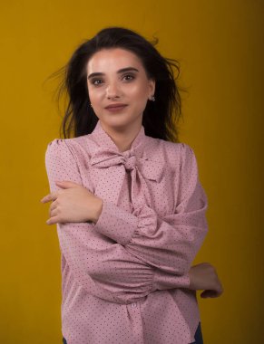 Pembe kazaklı genç güzel esmer manken, gülüyor ve saçlarını havada sallıyor, arkasında sarı arka plan, çok tatlı görünüyor, stüdyoda poz veriyor.,