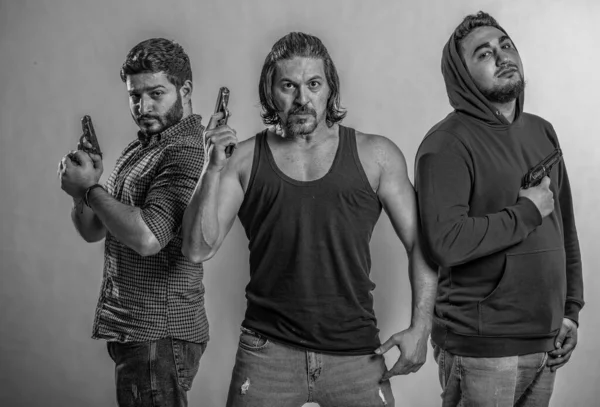 Silahlar üç gangsterin elinde, kızgın kameraya bakıyorlar, siyah tişört giymiş, mafya tarafından kutsanmış.,