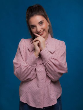 Pembe süveter giyen genç, güzel esmer model, arkasında mavi arka plan, okşama çok tatlı görünüyor, stüdyoda poz veriyor.,