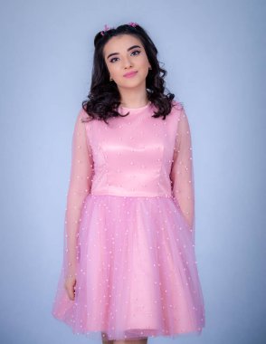 Mavi arka planda duran güzel bir kızın portresi, pembe elbiseli bir kız, mutlu gülümseyen tatlı bir kız yalnız poz veriyor.,