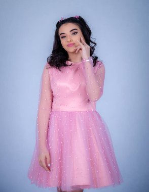 Mavi arka planda duran güzel bir kızın portresi, pembe elbiseli bir kız, mutlu gülümseyen tatlı bir kız yalnız poz veriyor.,