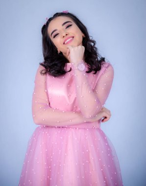 Mavi arka planda duran güzel bir kızın portresi, pembe elbiseli bir kız, mutlu gülümseyen tatlı bir kız yalnız poz veriyor.,
