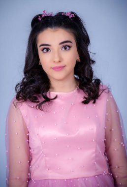 Mavi arka planda duran güzel bir kızın portresi, pembe elbiseli bir kız, mutlu gülümseyen tatlı bir kız yalnız poz veriyor.,