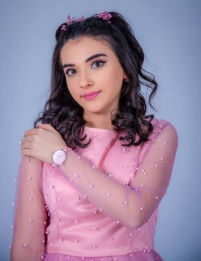 Mavi arka planda duran güzel bir kızın portresi, pembe elbiseli bir kız, mutlu gülümseyen tatlı bir kız yalnız poz veriyor.,