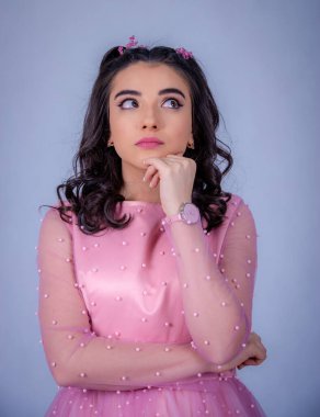 Mavi arka planda duran güzel bir kızın portresi, pembe elbiseli bir kız, mutlu gülümseyen tatlı bir kız yalnız poz veriyor.,