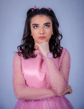 Mavi arka planda duran güzel bir kızın portresi, pembe elbiseli bir kız, mutlu gülümseyen tatlı bir kız yalnız poz veriyor.,