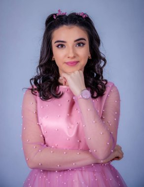 Mavi arka planda duran güzel bir kızın portresi, pembe elbiseli bir kız, mutlu gülümseyen tatlı bir kız yalnız poz veriyor.,