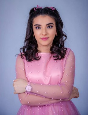 Mavi arka planda duran güzel bir kızın portresi, pembe elbiseli bir kız, mutlu gülümseyen tatlı bir kız yalnız poz veriyor.,