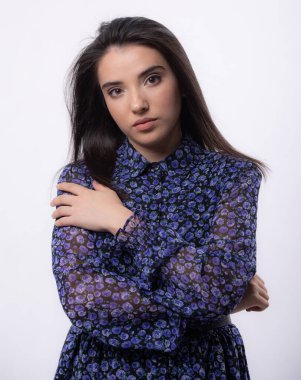 Stüdyoda poz veren mavi elbiseli mutlu kadın beyaz arka planda izole edilmiş, uzun saçlı, düşünceli bir şekilde kameraya bakıyor.,