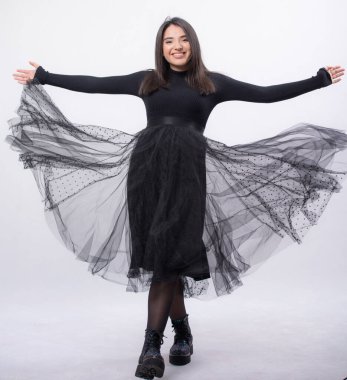 Stüdyoda poz veren mavi elbiseli mutlu bir kadın beyaz arka planda izole edilmiş, siyah uzun botları ayaklarında, tam boy portresi, gülümseyerek kollarını açtı.,