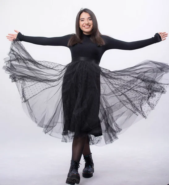 Stüdyoda poz veren mavi elbiseli mutlu bir kadın beyaz arka planda izole edilmiş, siyah uzun botları ayaklarında, tam boy portresi, gülümseyerek kollarını açtı.,