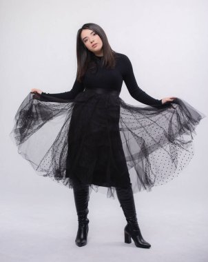 Stüdyoda poz veren mavi elbiseli mutlu bir kadın beyaz arka planda izole edilmiş, siyah uzun botları ayaklarında, tam boy portresi, gülümseyerek kollarını açtı.,