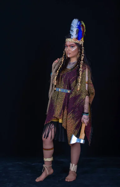 Native american. Indian woman in traditional dress posing in a studio,portrait of shamanic female with Indian feather hat and colorful makeup,holding an ax in his hands,