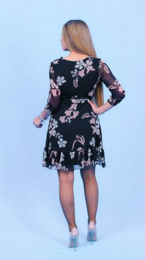 Mavi stüdyo arka planında izole edilmiş şık bir elbise giymiş çekici genç sarışın bir model. Güzel bir kız şık kıyafetler içinde kameraya bakıyor.,