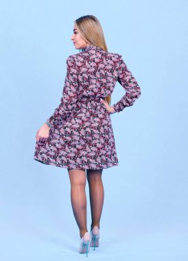 Mavi stüdyo arka planında izole edilmiş şık bir elbise giymiş çekici genç sarışın bir model. Güzel bir kız şık kıyafetler içinde kameraya bakıyor.,