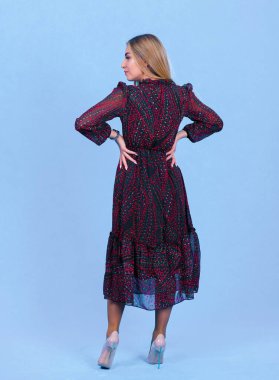 Mavi stüdyo arka planında izole edilmiş şık bir elbise giymiş çekici genç sarışın bir model. Güzel bir kız şık kıyafetler içinde kameraya bakıyor.,