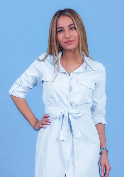 Mavi stüdyo arka planında izole edilmiş şık bir elbise giymiş çekici genç sarışın bir model. Güzel bir kız şık kıyafetler içinde kameraya bakıyor.,