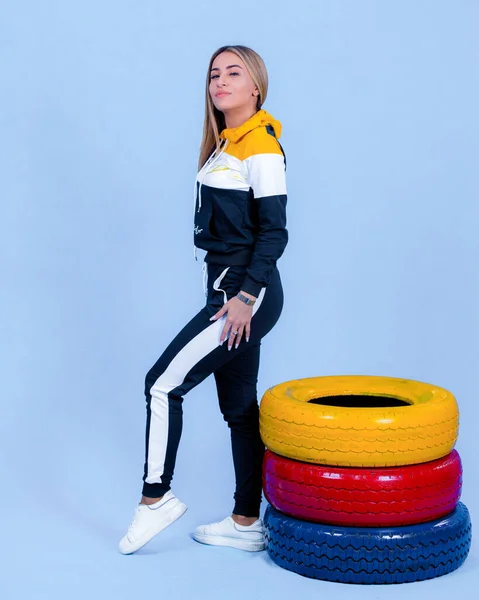 Hübsche Junge Blonde Modelmädchen Sportbekleidung Posiert Neben Autoreifen Blauem Hintergrund — Stockfoto