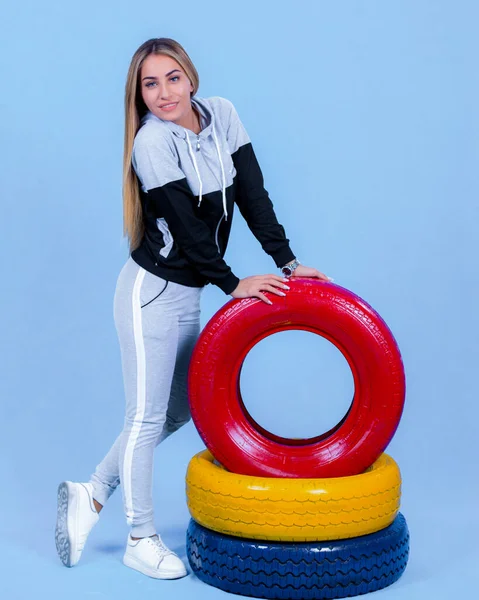 Hübsche Junge Blonde Modelmädchen Sportbekleidung Posiert Neben Autoreifen Blauem Hintergrund — Stockfoto