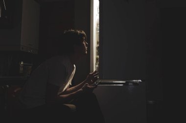 Gece karanlığında beyaz tişörtlü bir adam karantinada kendini izole ederek buzdolabının içine baktı.