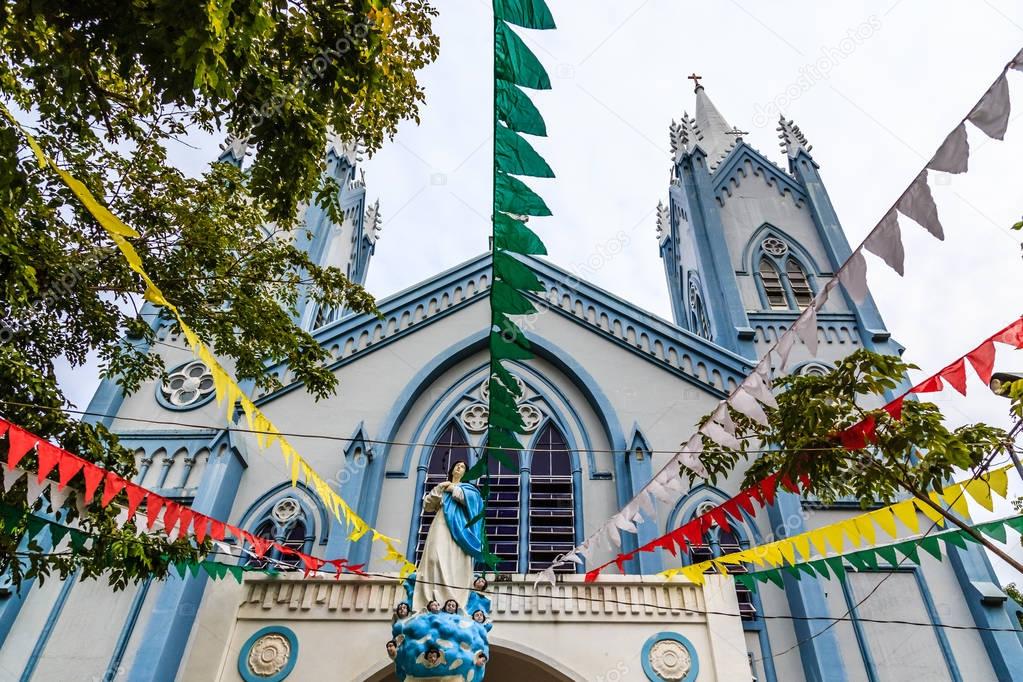 Blue Catholic church decorated with flags and Saint Mary statue 