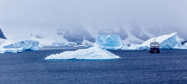 Sněžení a výletní loď mezi modré ledovce v Port Charcot, Bo — Stock fotografie