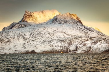 Büyük Sermitsiaq dağı, gün batımında mavi deniz ve Grönland yakınlarındaki Nuuk şehrinde küçük bir balıkçı teknesiyle kaplı karla kaplı.