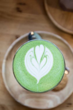 Ahşap masa arkasında kibrit yeşil çay latte sanat.