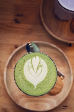 Ahşap masa arkasında kibrit yeşil çay latte sanat.