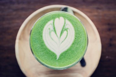 Ahşap masa arkasında kibrit yeşil çay latte sanat.