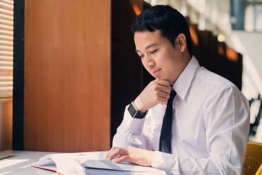 Genç Asyalı adam pencerenin yanındaki odada kitap okuyor..